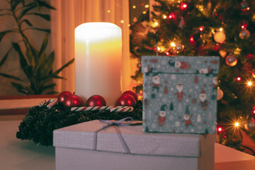 Christmas eve concept. Burning candle, gift boxes and festive lights.