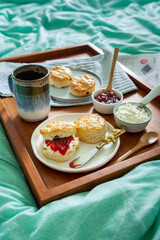 Home made scones with strawberry jam, clotted cream served in bed on a wooden tray with coffee and...