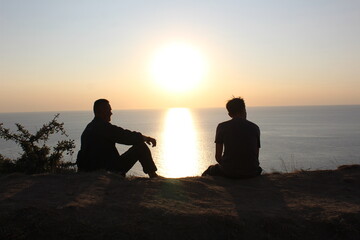 silhouette of two men sitting on the beach looking at the sunset