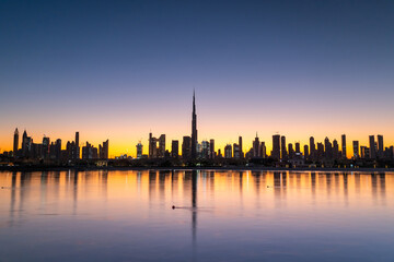 Fototapeta premium Sunrise in Dubai with clean blue sky view from boat or sea. The Sun rises over UAE skyscrapers at morning. Dubai beach, coast, shore
