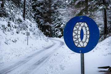 Frozen slippery road covered with snow through alpine forest. Chains on wheels sight.
