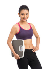 Beautiful smiling young fitness woman in tracksuit holding weigh scale over white background