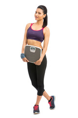 Beautiful smiling young fitness woman in tracksuit holding weigh scale over white background