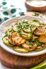 Fried zucchini with parsley, garlic, and sauce in a white ceramic plate close-up. Vegetarian snack.