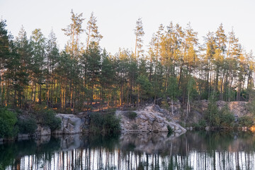 View of a beautiful flooded granite quarry with blue water among a pine forest on a sunny summer day