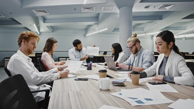 Manager discussing details of new startup with diverse colleagues, sitting at table in modern office
