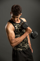 Fototapeta na wymiar muscular young man lifting weights for biceps curl on dark background.