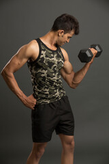 muscular young man lifting weights for biceps curl on dark background.