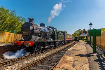 Steam trains passing at a station on a railway line in Sussex, UK on a sunny summer day