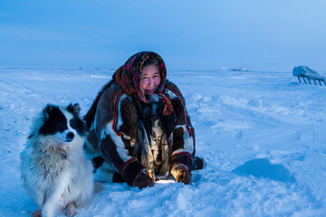 A woman, in the national winter clothes of the northern inhabitants of the tundra, plays with a dogs in minus 40, in the polar night