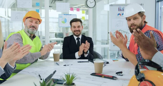 Close up of good-looking smiling satisfied experienced professional mixed race team of builders and their male and female bosses which applauding after successful ending of construction project