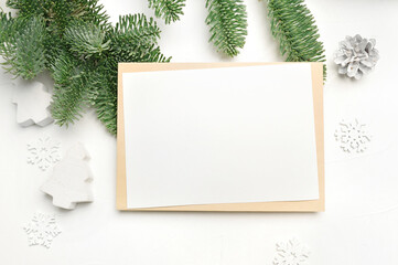 Mockup Christmas greeting card with envelope on wooden white background with fir tree branches and happy new year decorations. Top view copyspace