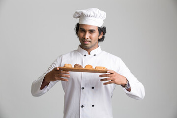 surprised male chef posing with cookies isolated over grey gradient background