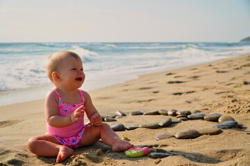 Happy baby in the sand plays. Cheerful little kid playing on the beach on a sunny day. High quality photo