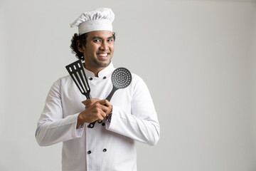 Naklejka premium Cheerful happy chef holding kitchen utensil isolated on grey background
