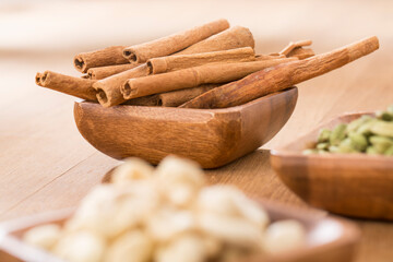 wooden bowl of cardamom, cinnamon and cashew on wooden table.