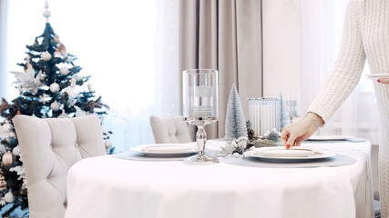 A girl in a white dress serves plates at the Christmas table. Festive table setting
