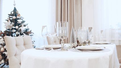 A girl in a white dress serves wine glasses at the Christmas table. Festive table setting