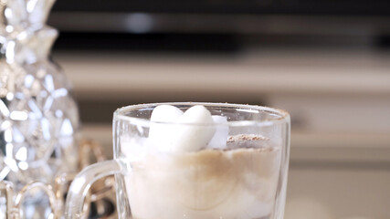 Female fingers poke marshmallows that float in coffee