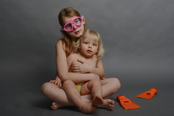 older sister and young brother are having fun, children in swimsuits put on fins