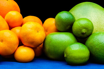 Isolated orange and green color groups citruses fruits on black background. Oranges, tangerines, limes, pummelo, grapefruits on blue tablecloth