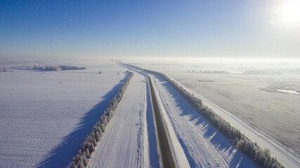 Winter road along the fields between cities aerial view from a drone. Winter road view from a drone