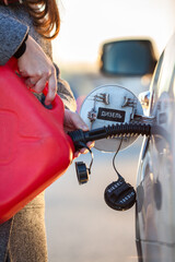 Female driver pouring diesel from red plastic oil can into empty car tank, close-up view