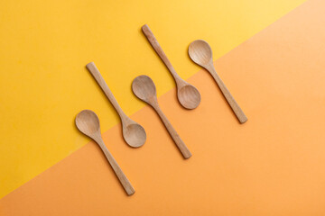 Group of five empty wooden spoons on orange and yellow background, top view with copy space. Zero waste, eco-friendly kitchen utensils made of bamboo, sustainable lifestyle concept