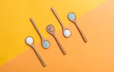 Group of five wooden spoons with different kind of salt on orange and yellow background, top view with copy space.Zero waste, eco-friendly kitchen utensils, sustainable lifestyle concept