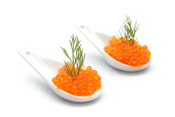 Closeup of trout roe in a ceramic spoon with a dill leaf on white background