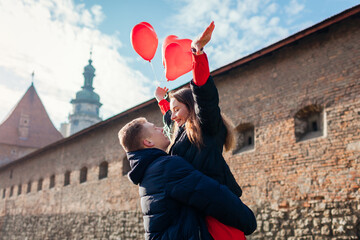 Valentines day couple. Man holding his girlfriend raising arms with balloons on city street. People having fun