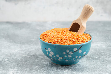 Bowl of raw red lentils on marble background with spoon