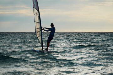 A man controls a sailing board on the sea. Copy space. Selective focus.