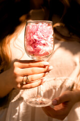 female hands hold a glass of wine with sakura petals. female hands with rings.