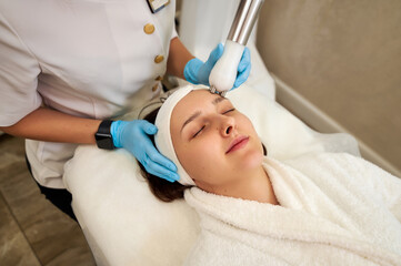 Beautiful woman receiving facial microcurrent treatment from beautician in beauty wellness salon .