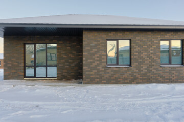 One-story brick house on the background of a snowy winter evening. Construction of low-rise buildings for further sale. Concept of building business.
