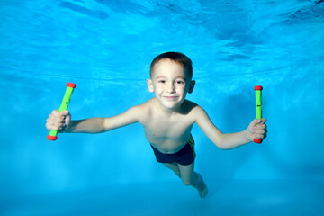 Portrait of a beautiful boy at the bottom of a children's pool. He smiles and looks into the camera frame. Fun dives underwater. Active happy child. Swimming classes. Bodily exercises