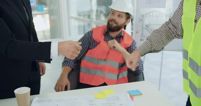 Unknown confident man in suit handshaking with professional experienced engineer in vest during meeting in boardroom about joint construction project