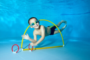 A beautiful little boy dives underwater in a children's pool. He swims through the Hoop, pulls out toys. Active happy child. Healthy lifestyle. Swimming lessons under the water. A family sport