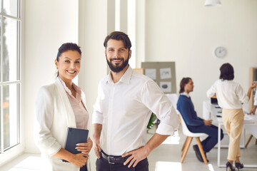 Portrait of confident woman and man standing in office hall against workers background.