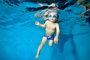 Portrait of a boy in a Santa hat and glasses in a pool underwater. The kid learns to have fun diving under water. Swimming lessons with a child. Healthy lifestyle. Horizontal orientation