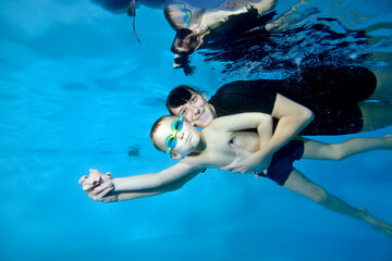 A beautiful boy and a female coach swim under the water with their arms outstretched. They smile...
