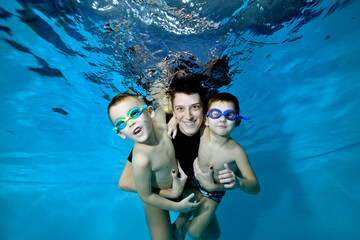 Two beautiful boys underwater with their mother. She hugs them tenderly. They smile and look at the...