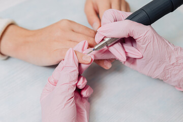 Manicure process. A master in pink rubber gloves polishes nails with an electric nail file. Female hands close up.