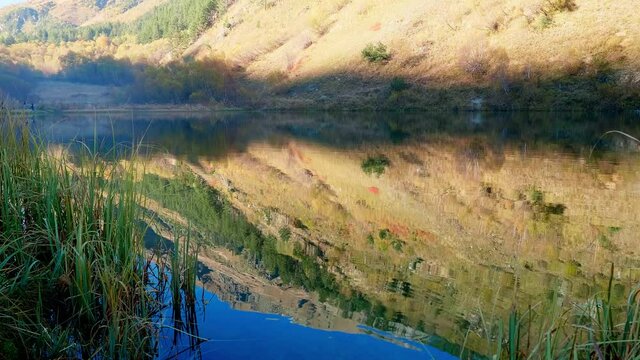 Reflection of mountain side covered with dry yellow grass in mountain lake. Sunny autumnn wamr day with nice weather.