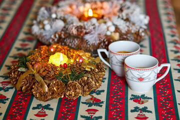 New Year's table with coffee covered with a red tablecloth, a decorated candle in a candlestick with spruce branches and shyshys covered with snow.