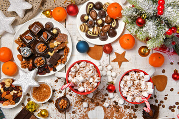 sweet food top view background for merry christmas or new year holiday decoration - chocolate candies, tangerines, cookies, marshmallow and cocoa latte on white wood