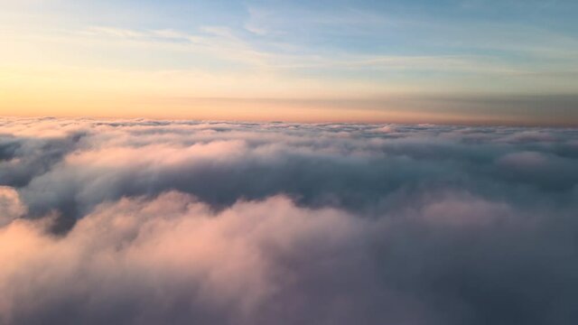 Aerial view of vibrant yellow sunrise over white dense clouds with blue sky overhead.