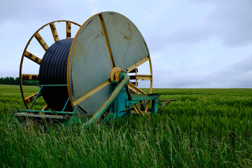Vintage farming equipment with a industrial watering hose in a large coil in middle of a field