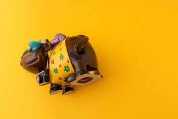 A brown cow smiling toy, wearing a blue hat, a bag and a camera, with yellow background.concept of travel.